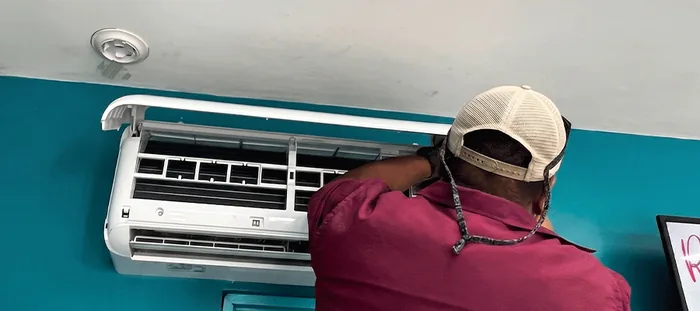 Tecnico de Kosago Corp dando mantenimiento a un aire acondicionado tipo split montado en la pared